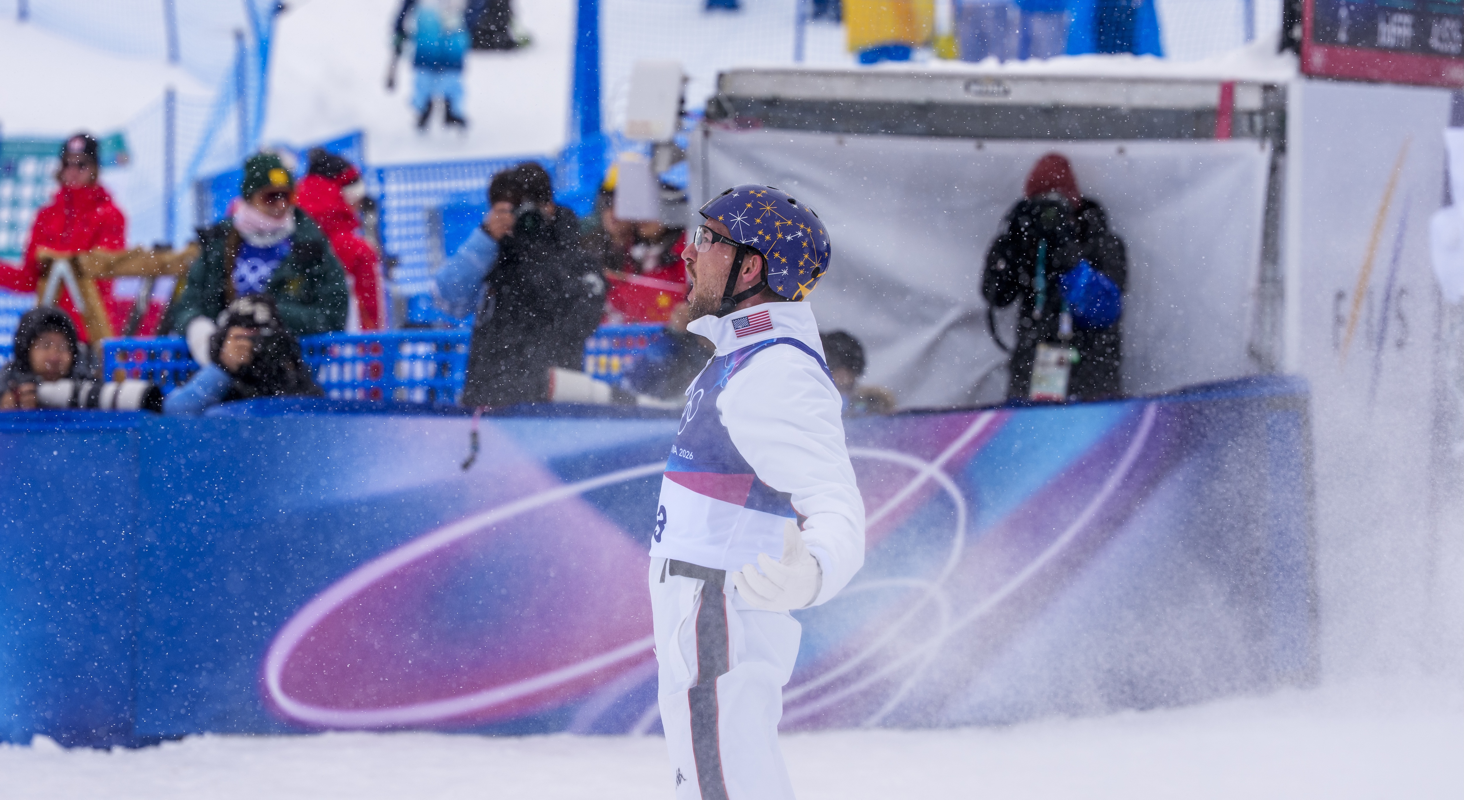 Chris Lillis celebrates in the finish area after landing his jump in the team event at the 2026 Olympic Winter Games